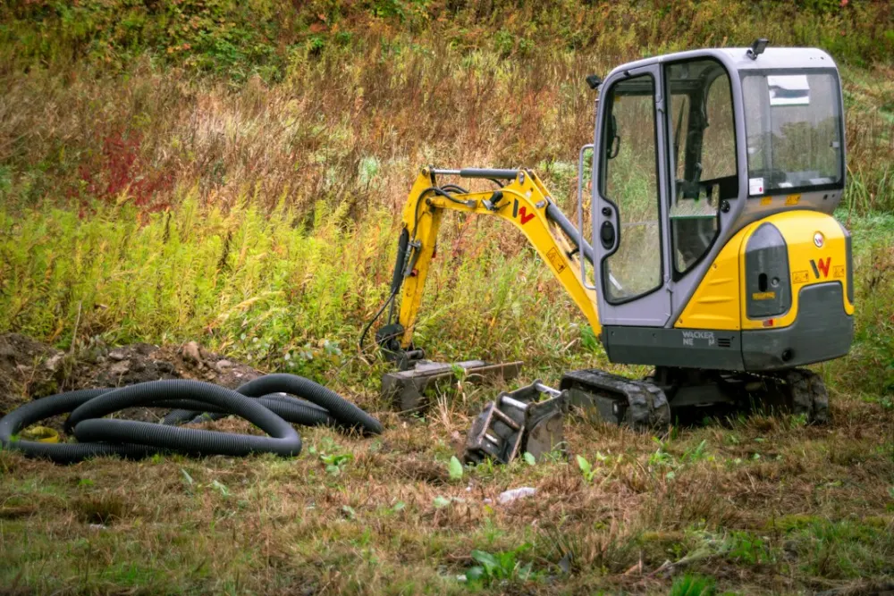 Mini excavator on the site next to a coiled protective sleeve ready for installation in the trench.